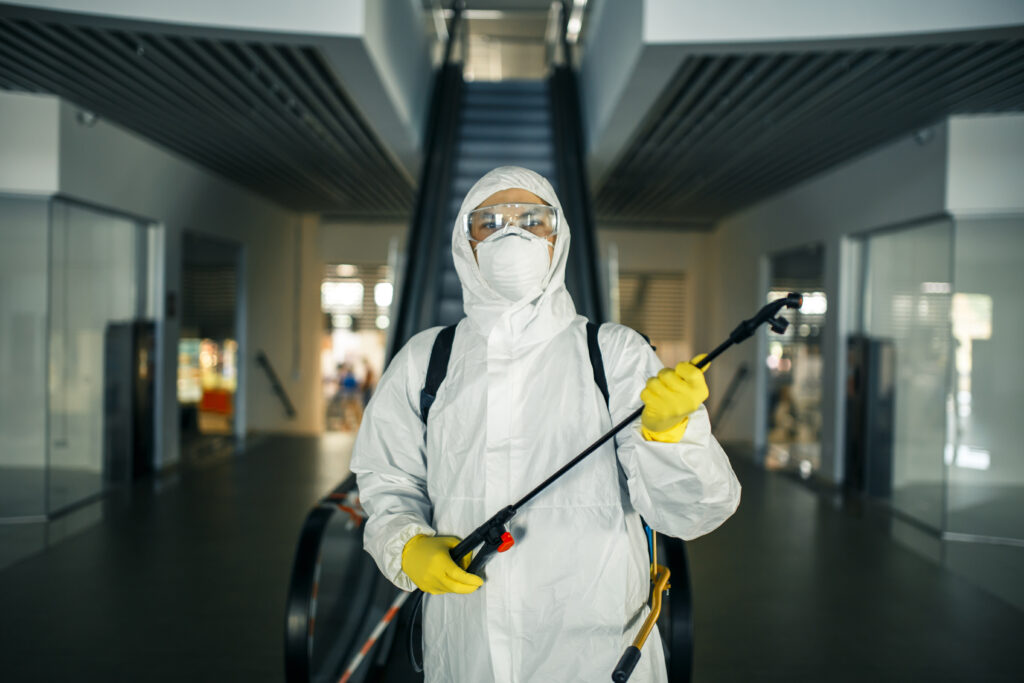 portrait of a man in a sanitizing disifection suit holding spray near the escalator in an empty shopping mall. a volunteer cleaning up the public places to prevent covid 19. health awareness concept.